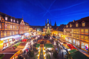 Weihnachtsmarkt in Werningerode bei Nacht: Blick auf den festlich beleuchteten Marktplatz mit Buden, Weihnachtsbaum und Fachwerkhäusern. Menschen bummeln durch den Markt, genießen die Atmosphäre.