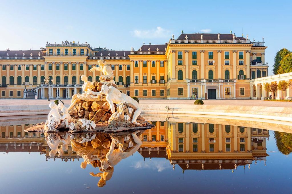 Schloss Schönbrunn in Wien mit dem Schloßbrunnen als zentrales Motiv. Die gelbe Schlossfassade aus dem Barock spiegelt sich im Brunnenbecken.