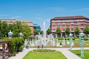 In der Wasserturmanlage in der Innenstadt von Mannheim befindet sich ein großer Springbrunnen. Gepflegte Grünflächen und historische Gebäude umgeben diesen.