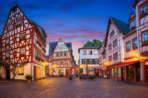 Fachwerkhäuser umringen in der Mainzer Innenstadt einen kleinen Platz, der am Abend von Laternen beleuchtet wird.