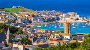 Malerische Aussicht auf St Ives, Cornwall, mit Häusern mit orangefarbenen Dächern, einem Hafen voller Boote und einer Kirche mit Turm. Ideal für den Reisekatalog 2026.