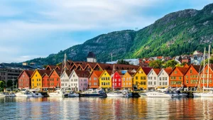 Bryggen in Bergen, Norwegen: Bunte Holzhäuser am Hafen unter einem grünen Berg, reflektiert im Wasser. Ein Blick aus dem neuen Reisekatalog 2026.