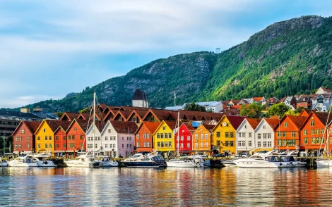 Bryggen in Bergen, Norwegen: Bunte Holzhäuser am Hafen unter einem grünen Berg, reflektiert im Wasser. Ein Blick aus dem neuen Reisekatalog 2026.
