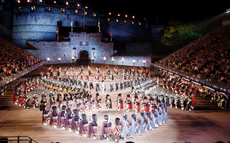 Nachtszene des Edinburgh Military Tattoo vor dem erleuchteten Edinburgh Castle. Dudelsackspieler und Tänzer in traditionellen schottischen Trachten treten vor einer großen Zuschauermenge auf.