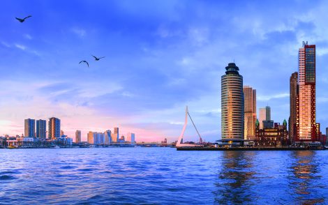 Panorama von Rotterdam bei Sonnenuntergang. Moderne Architektur, Erasmusbrücke und ruhiges Wasser in warmen Farben.