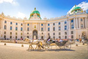 Pferdekutsche vor der Hofburg in Wien, Österreich, mit Touristen und strahlend blauem Himmel. Elegante Architektur und ein Hauch von historischem Charme.