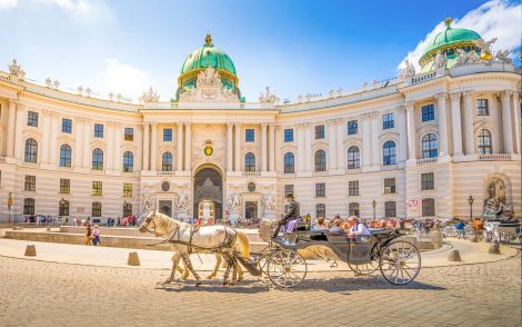 Pferdekutsche vor der Hofburg in Wien, Österreich, mit Touristen und strahlend blauem Himmel. Elegante Architektur und ein Hauch von historischem Charme.