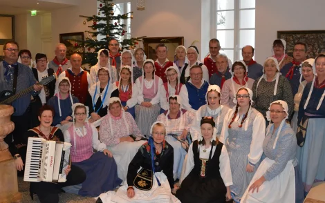 Große Gruppe in Trachten namens „Sohl’nborger Büttpeddern“ von Rügen, posiert mit Akkordeon und Gitarre vor Weihnachtsbaum. Traditionelle Kleidung, festliche Stimmung.