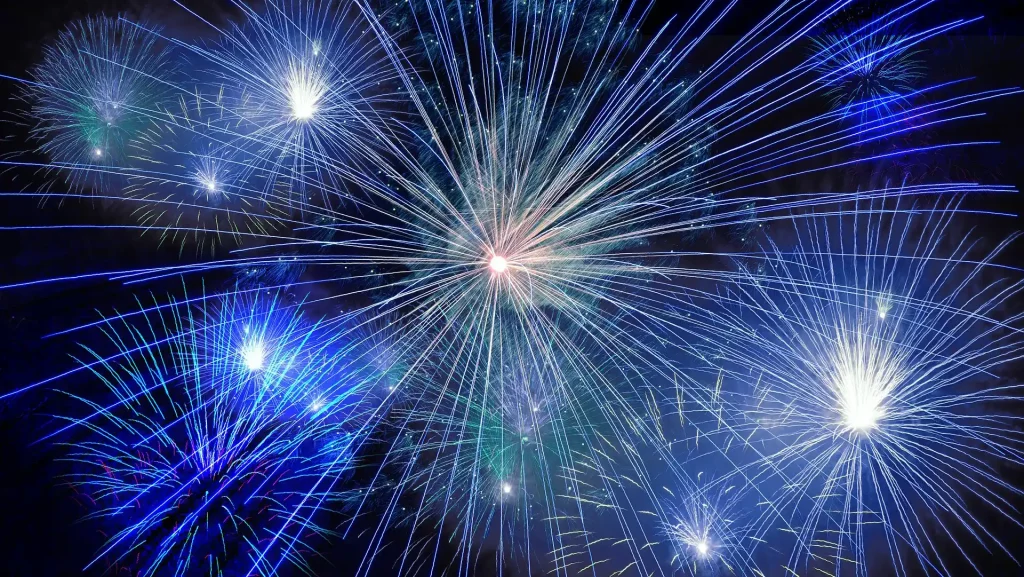 Funkelndes Feuerwerk mit blauen und weißen Sternen vor dunklem Nachthimmel.