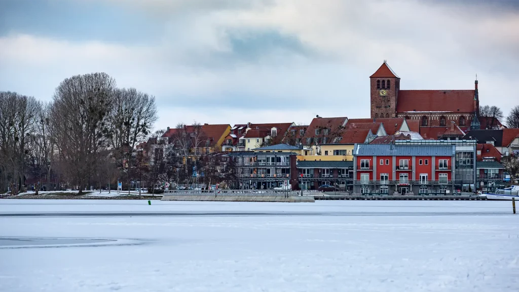 Winterliches Waren (Müritz) mit gefrorenem See und farbenfrohen Häusern am Ufer, im Hintergrund die Kirche.