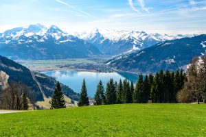 Schneebedeckte Berge und der Zellersee mit grünen Wiesen und Wäldern