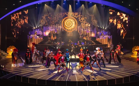 Große Bühne im Friedrichstadtpalast Berlin für die Grand Show „BLINDED by DELIGHT“: Tänzer in farbenprächtigen Kostümen vor einer riesigen Uhr und aufwendigen Bühnenbild.