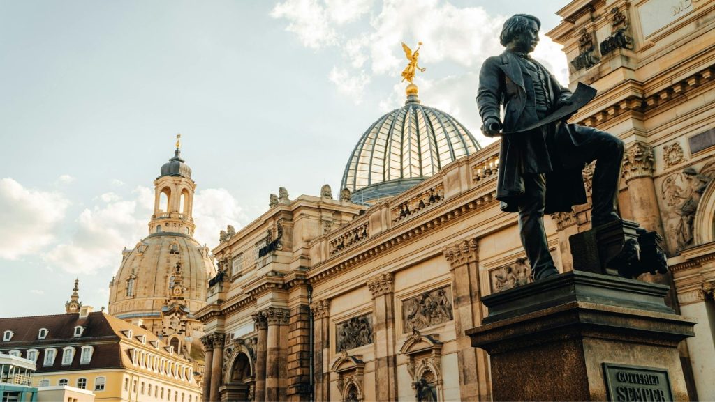 Dresden Ansicht: Semperoper Statue vor Kuppel und Frauenkirche. Goldene Details, helle Fassade, blauer Himmel. Gottfried Semper.