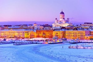 Winterliches Helsinki im Eis: Blick auf die schneebedeckte Stadt mit der strahlenden Kathedrale im Abendlicht. Boote liegen im gefrorenen Hafen.