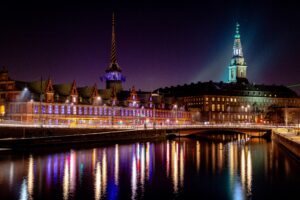 Nächtliche Ansicht von Kopenhagen, Dänemark, mit beleuchteten historischen Gebäuden, die sich im Wasser spiegeln. Stimmungsvolle Stadtlandschaft.