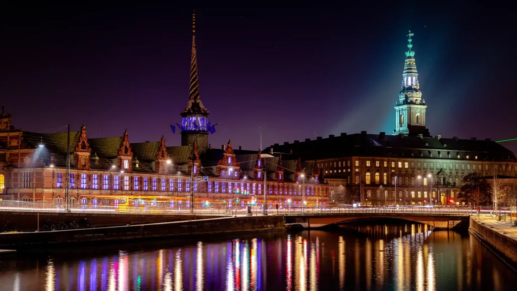 Nächtliche Ansicht von Kopenhagen, Dänemark, mit beleuchteten historischen Gebäuden, die sich im Wasser spiegeln. Stimmungsvolle Stadtlandschaft.