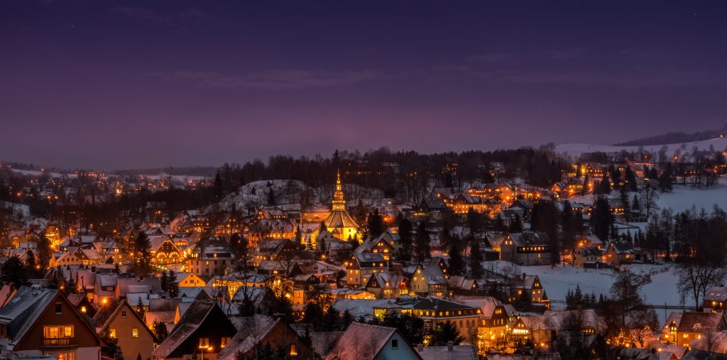 Winterliche Kleinstadt im Erzgebirge im Abendlicht mit schneebedeckten Dächern und beleuchteten Fenstern, eine Kirche mit Turm ragt hervor.