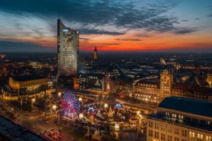 Leipziger Stadtbild bei Dämmerung mit beleuchtetem Riesenrad und Weihnachtsmarkt, im Hintergrund das markante City-Hochhaus.