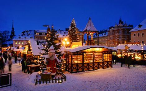 Verschneiter Weihnachtsmarkt im Erzgebirge bei Dämmerung, festlich beleuchtete Stände und Weihnachtsbäume, Glanzlichter.