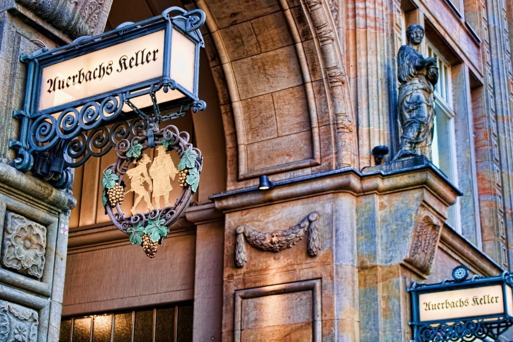 Detailaufnahme von Auerbachs Keller in Leipzig, einem historischen Restaurant. Geschmiedete Schilder mit dem Schriftzug "Auerbachs Keller" und einer Szene aus Goethes Faust. Architektur mit Sandsteindetails.