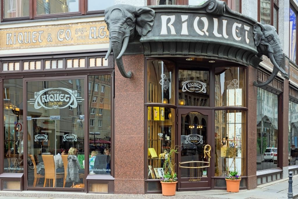 Fassade des Kaffeehauses Riquet in Leipzig mit Elefantenköpfen. Das Riquet, ein Wahrzeichen lebendiger Stadtkultur, lädt zum Verweilen ein. "RIQUET & CO. A.G." und "RIQUET Stadtcafé" sind auf der Fassade zu lesen.